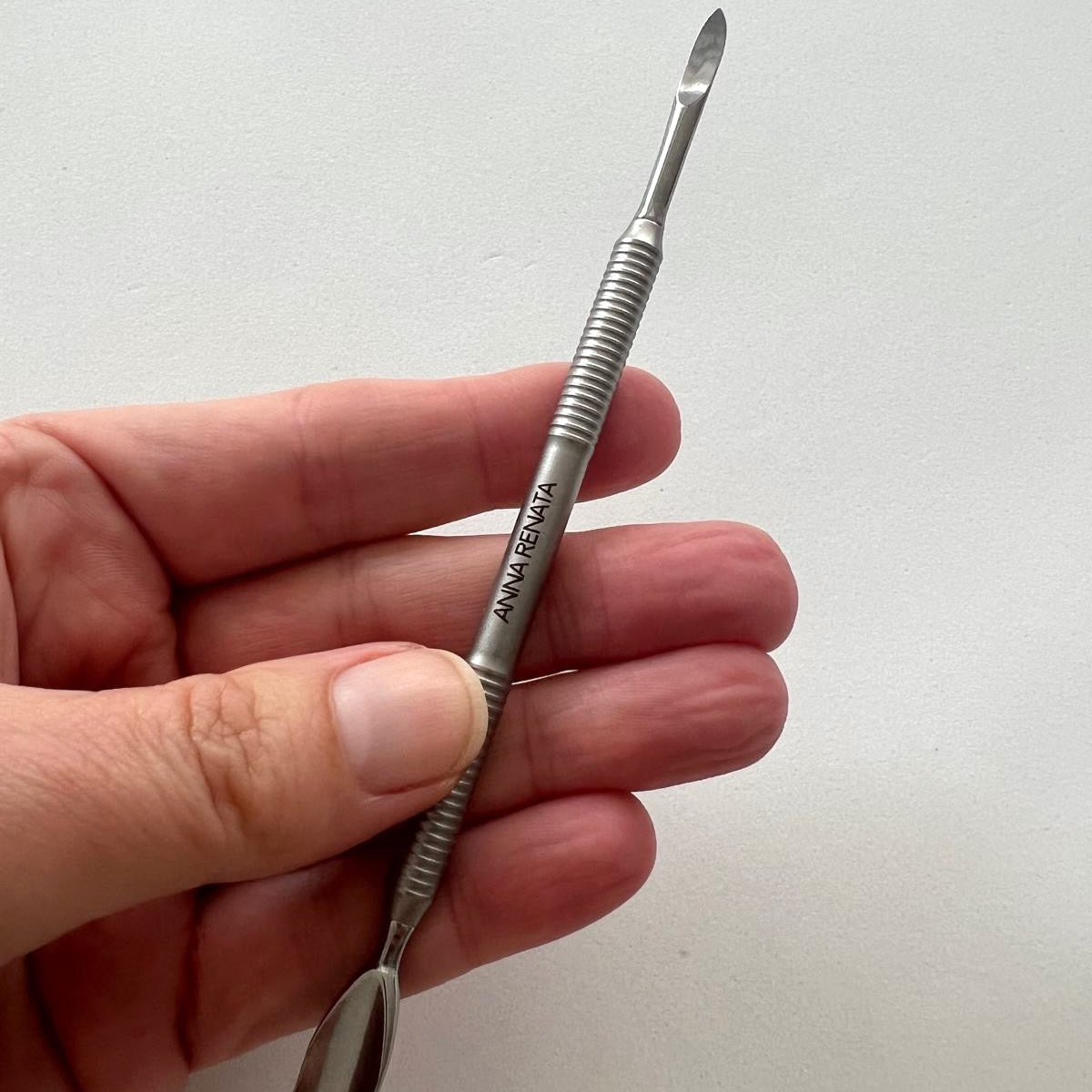 Hand holding a silver tool with Anna Renata branding on a white background